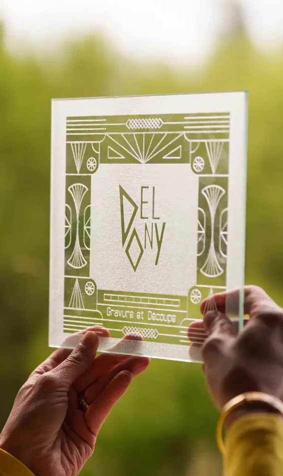 Plaque de verre gravée du logo Delony tenue à la lumière du jour