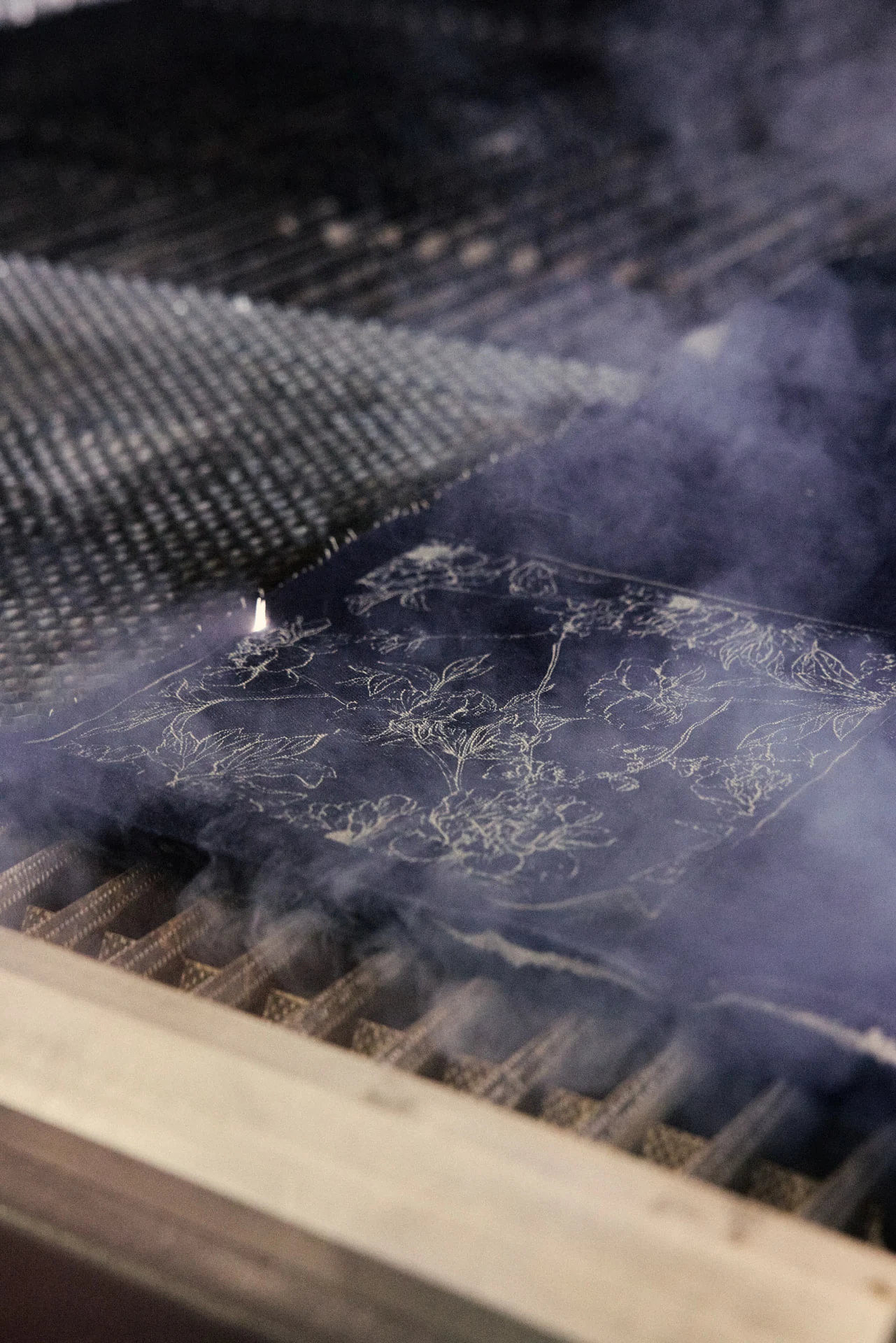 Motif floral gravé au laser sur denim indigo, dans la fumée de la machine
