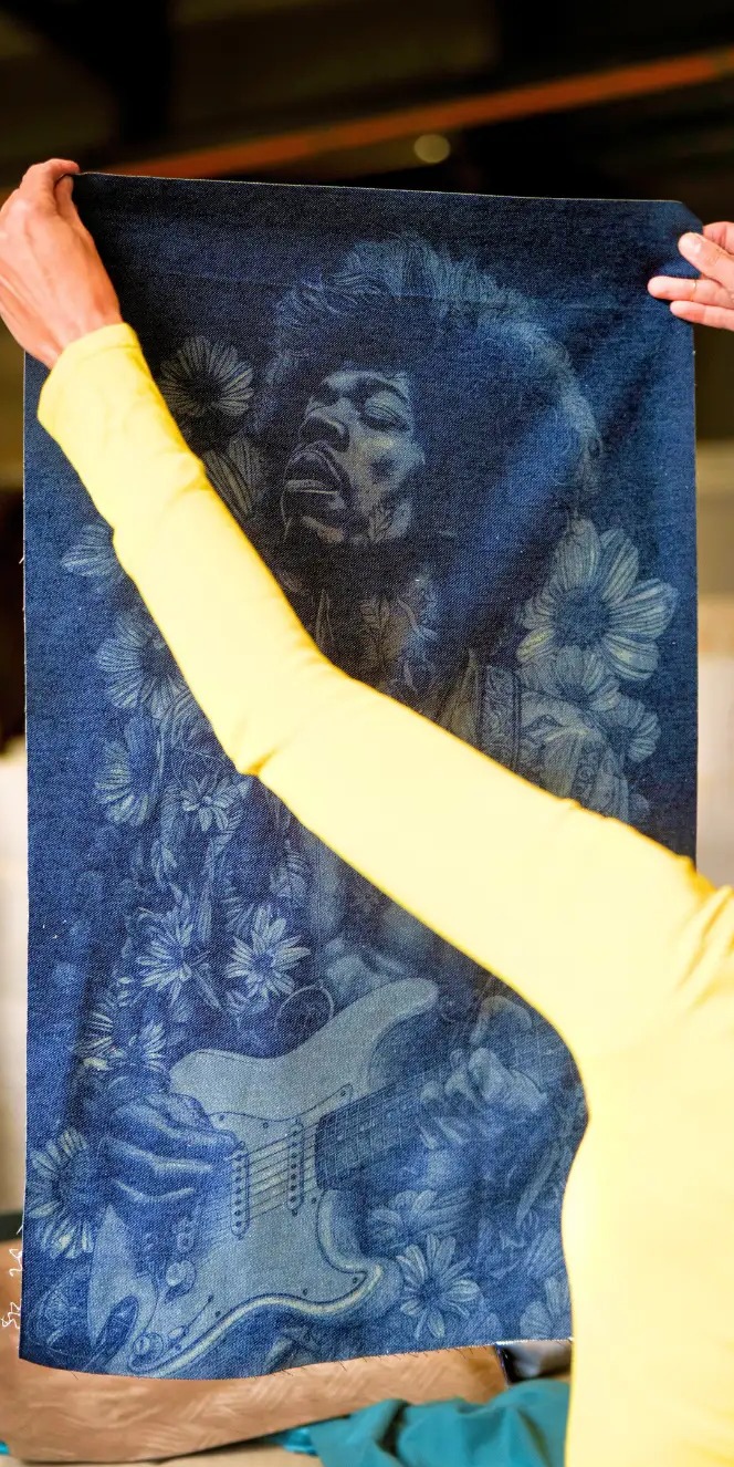 Toile de denim gravée au laser d'un portrait de guitariste, tenue à bout de bras dans l'atelier